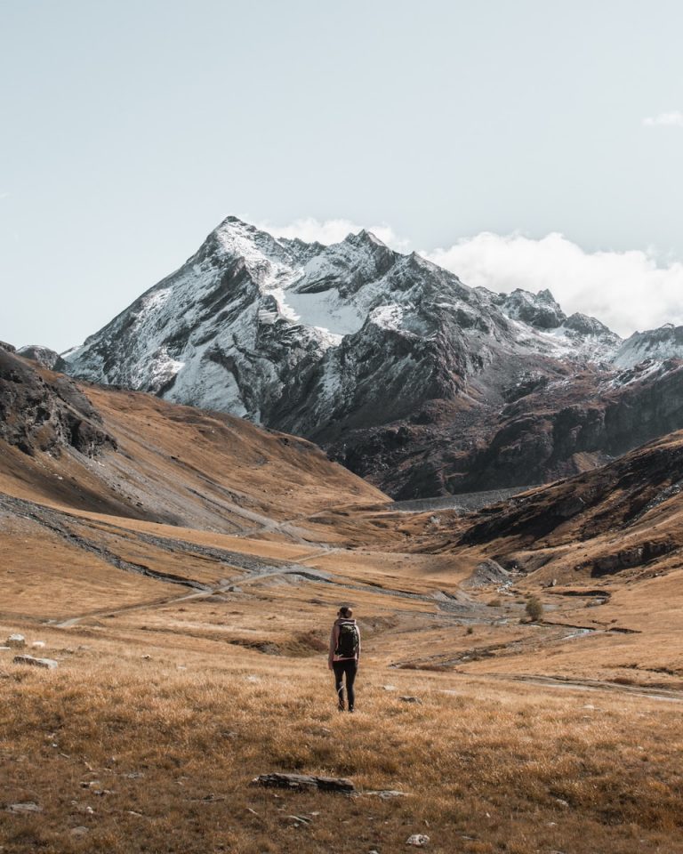 person standing on brown field viewing mountain under white and blue sky during daytime